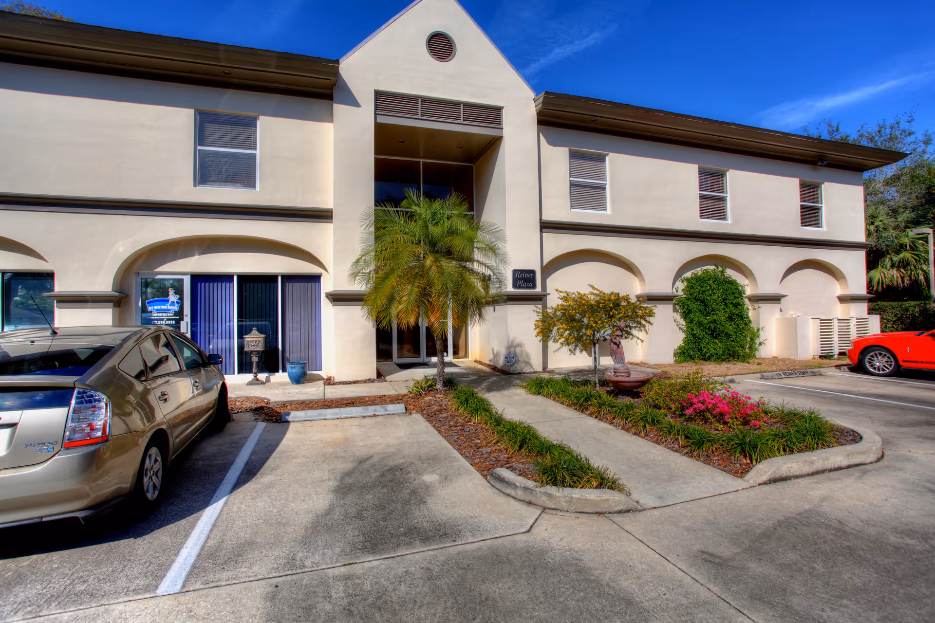 Two-story senior living facility front entrance with palm tree and parking.
