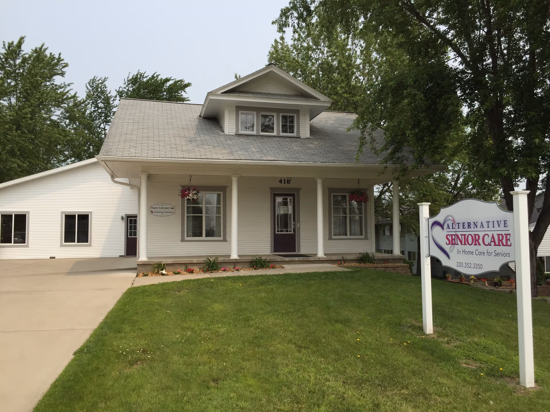 A white, single-story senior care facility with a front porch and sign.