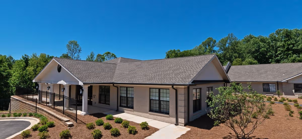 Exterior view of a single-story senior living facility with entrance, walkway, and landscaping.