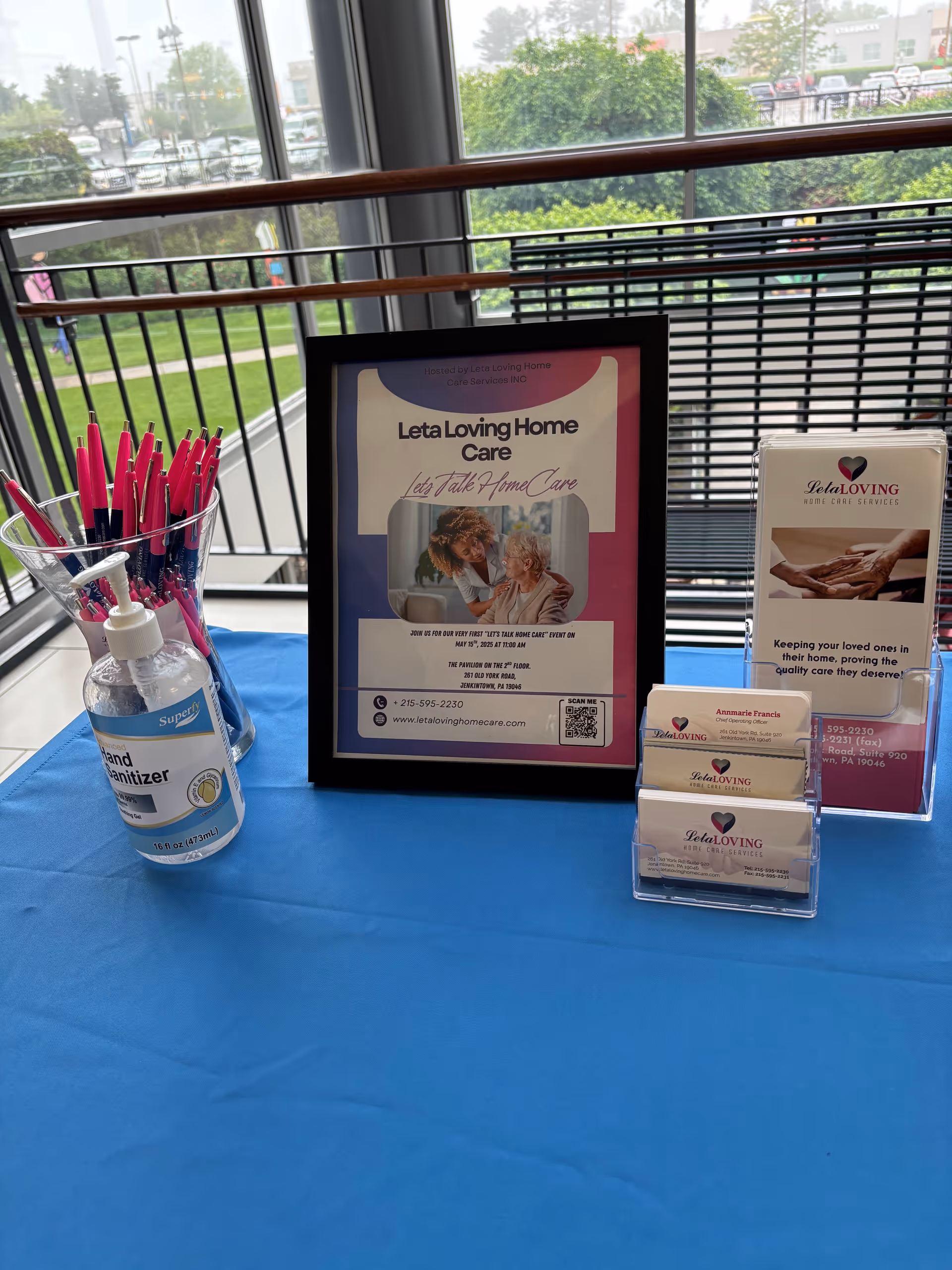 Framed Leta Loving Home Care poster on a blue table with brochures and sanitizer indoors.
