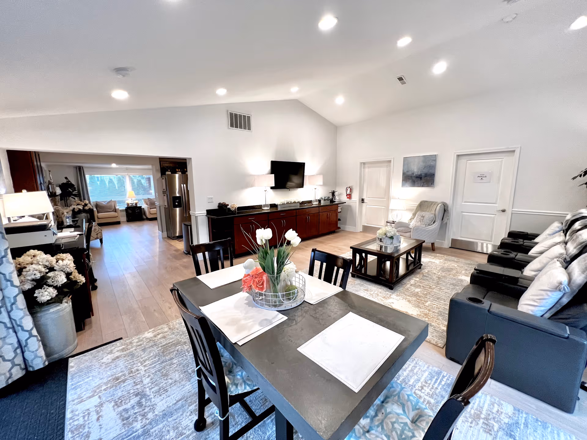 Spacious interior common area with dining table, seating, and a TV in a senior living facility.