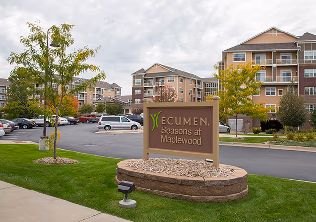 Exterior view of Ecumen Seasons at Maplewood with sign and surrounding buildings.