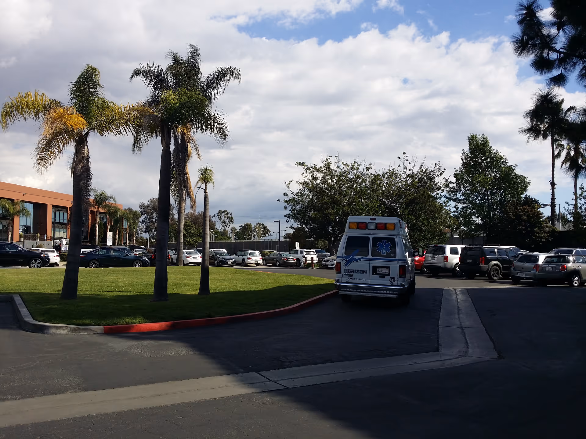 Parking lot in front of a building with palm trees and an ambulance.