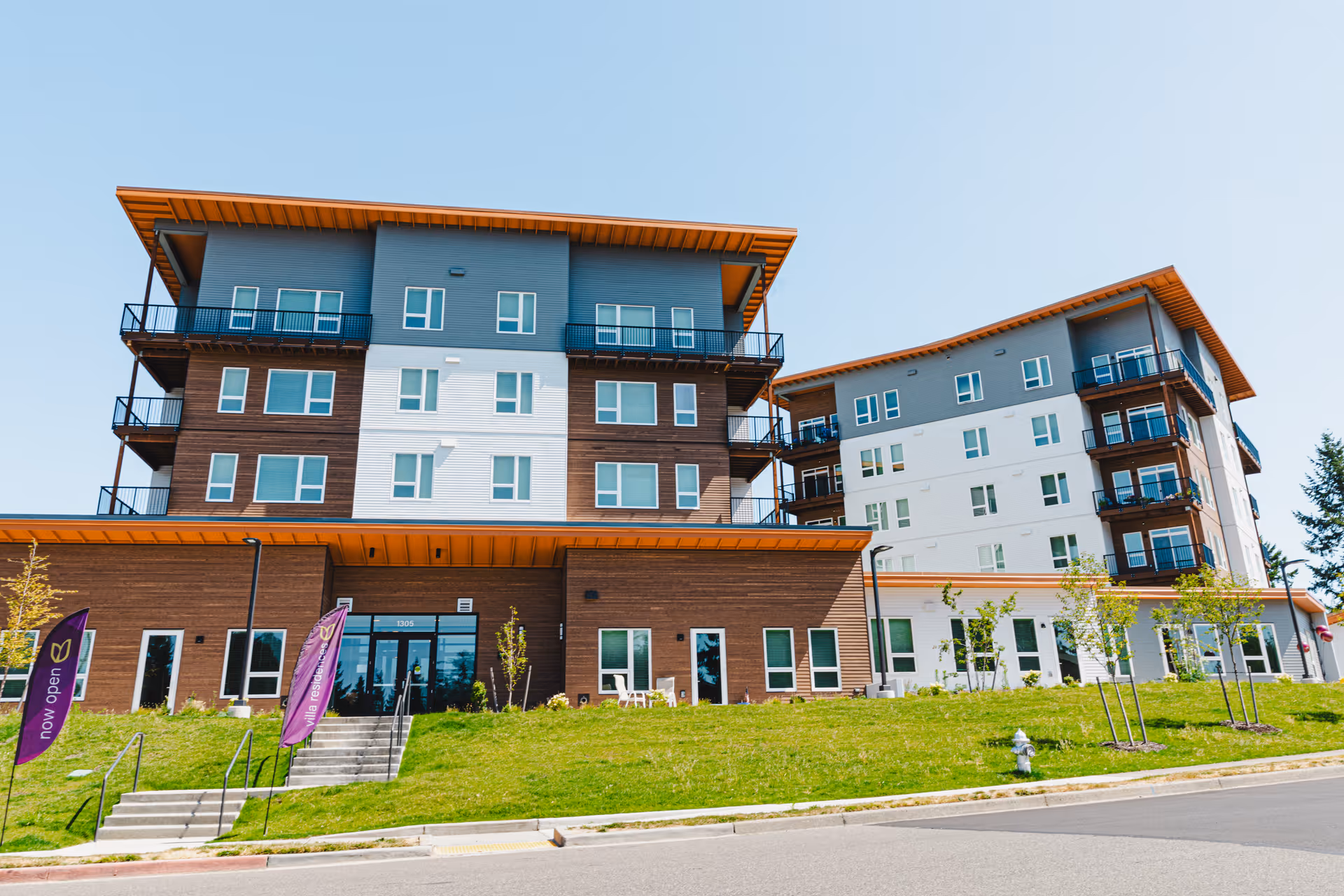 Exterior view of Eliseo senior living building with multiple stories, balconies, and a grassy approach.