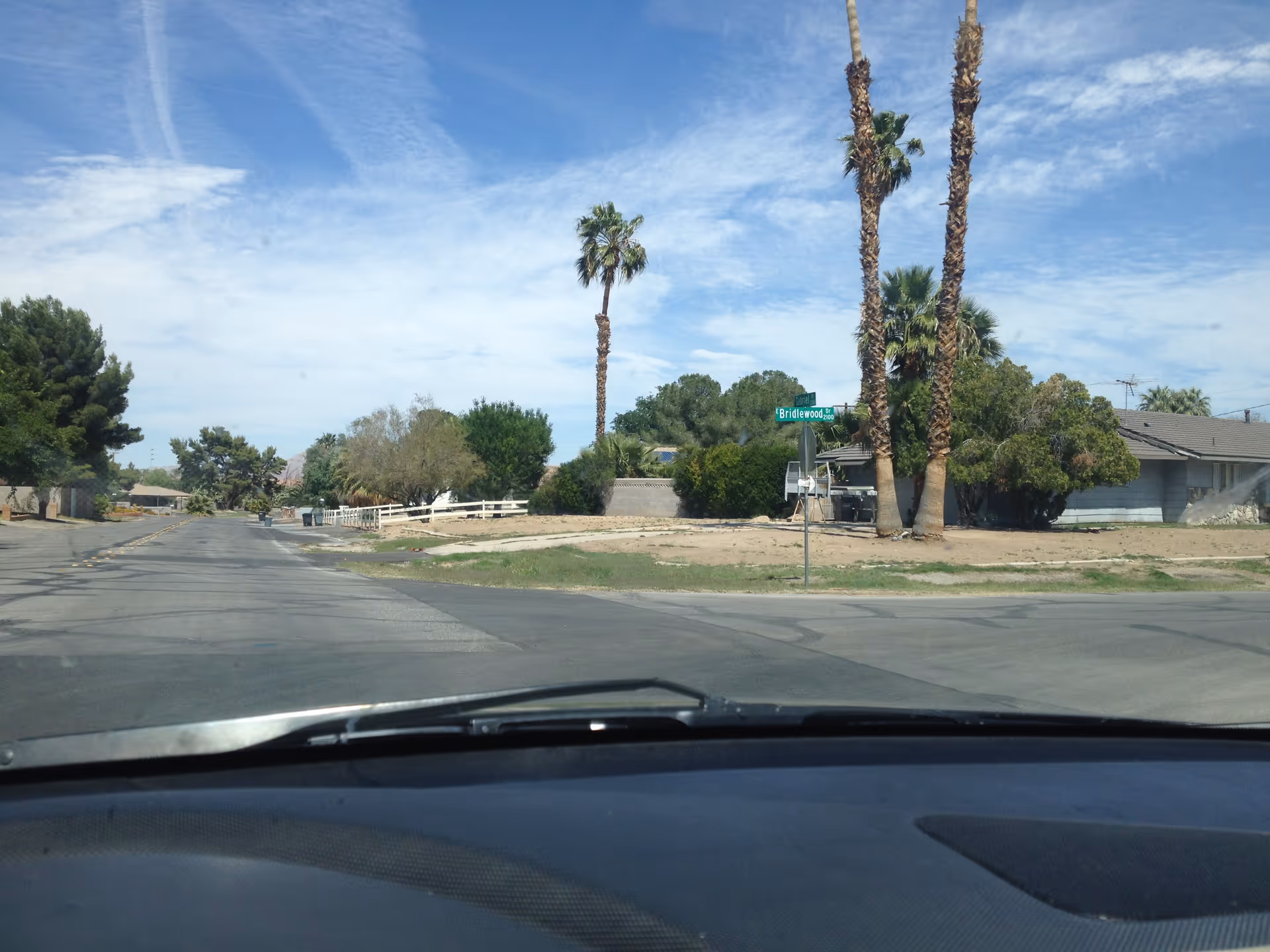 Wide street view of a desert neighborhood with palm trees and blue sky.