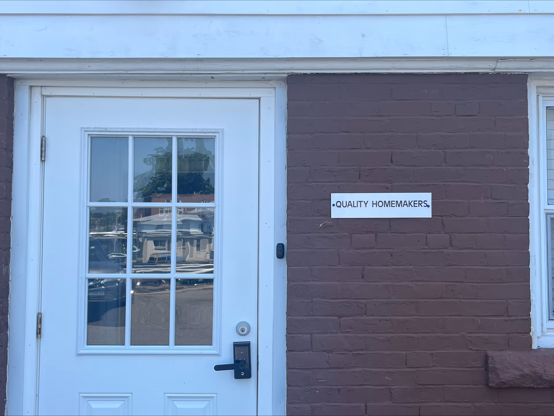 White door with glass panes beside brown brick wall and Quality Homemakers sign