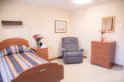 Resident bedroom with a single bed, nightstand with flowers, a recliner chair, and a dresser with mirror.