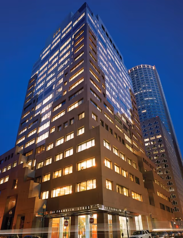 Tall modern high-rise building at dusk with illuminated windows and street entrance.