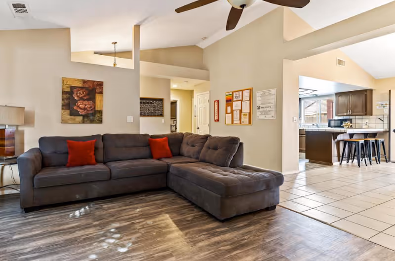 Open living room with gray sectional, red pillows, and adjacent kitchen.