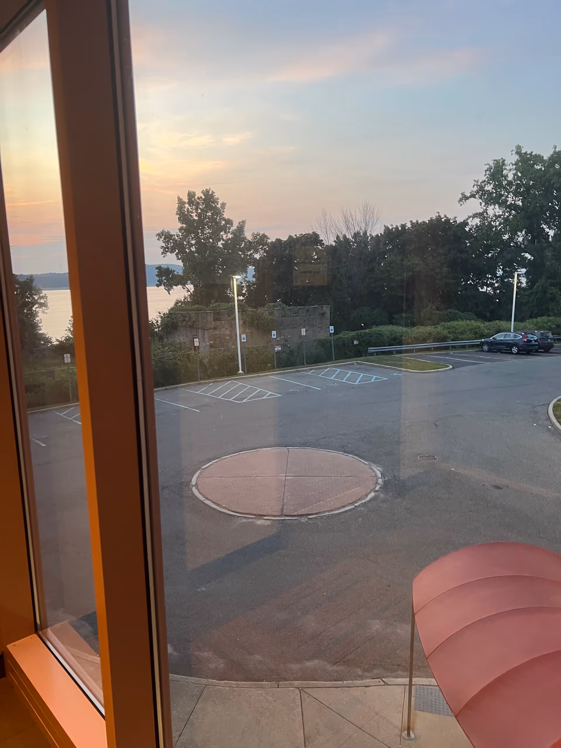 Interior window view of parking lot, trees, and sunset.