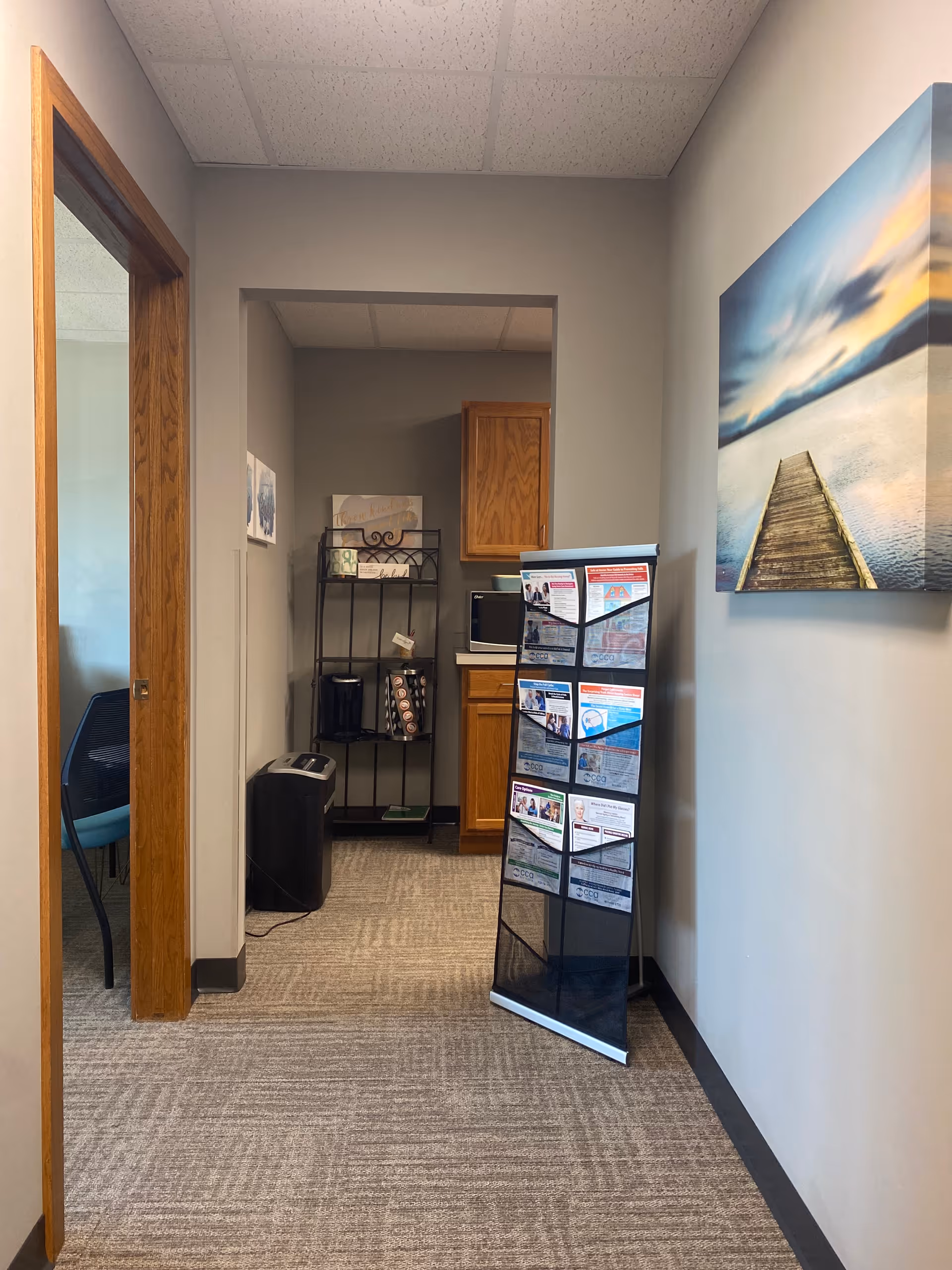 Interior hallway of a senior living facility with a brochure rack and wall art.