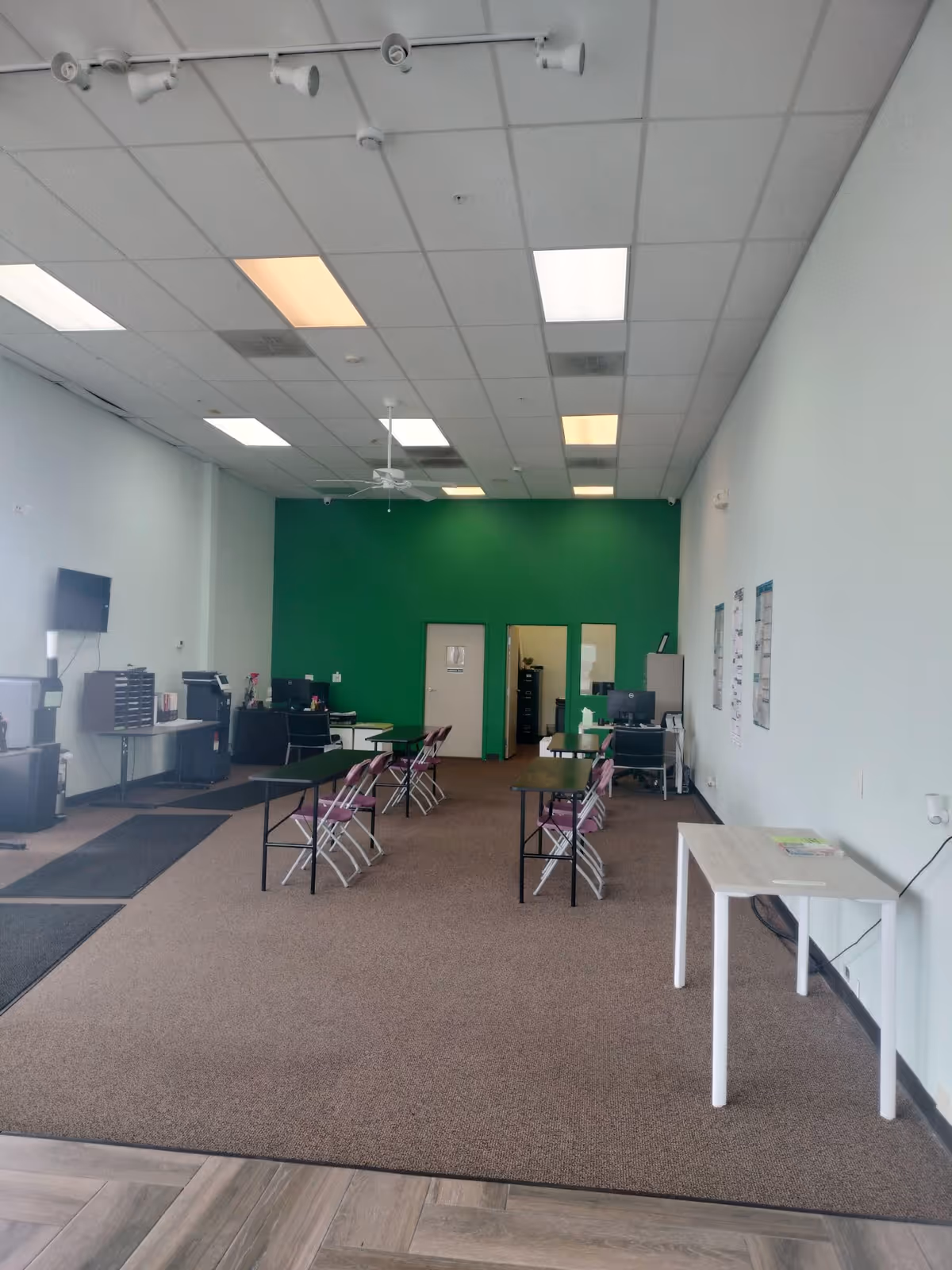 A spacious interior room with a green back wall, tables and pink folding chairs.