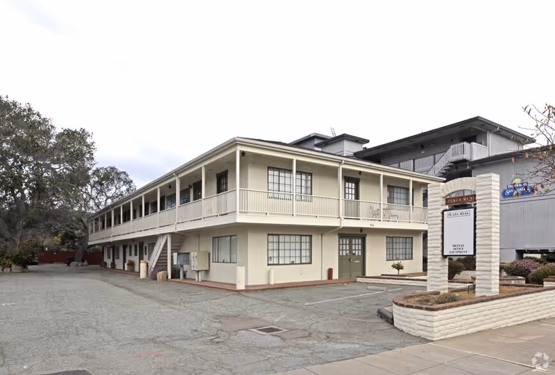 Exterior view of a two-story beige senior living building with a long balcony and parking lot.