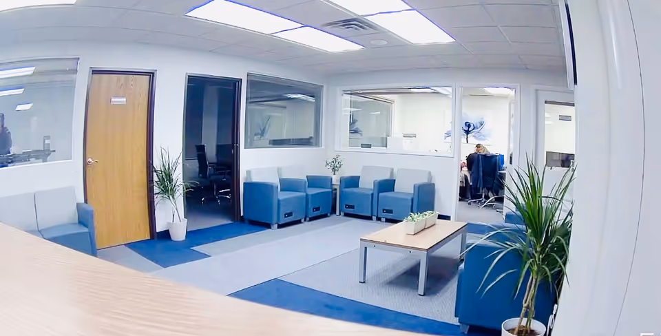 Bright lounge area with blue chairs, plants, and a coffee table.