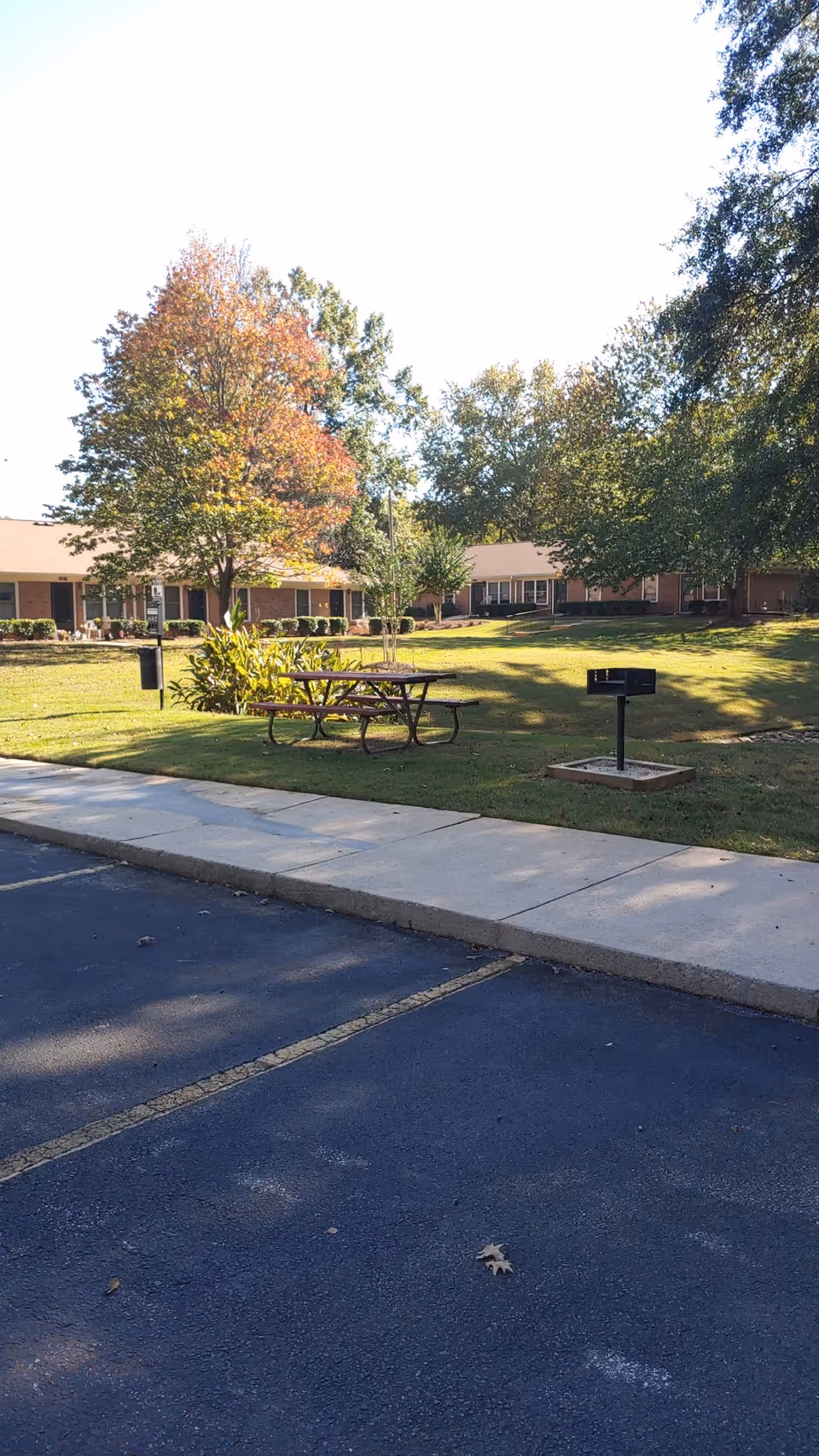 Outdoor lawn with picnic table, grill, and trees in front of a brick senior living building.