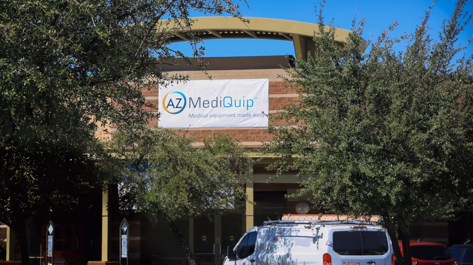 Exterior view of AZ MediQuip Goodyear with banner, trees, and a white van.