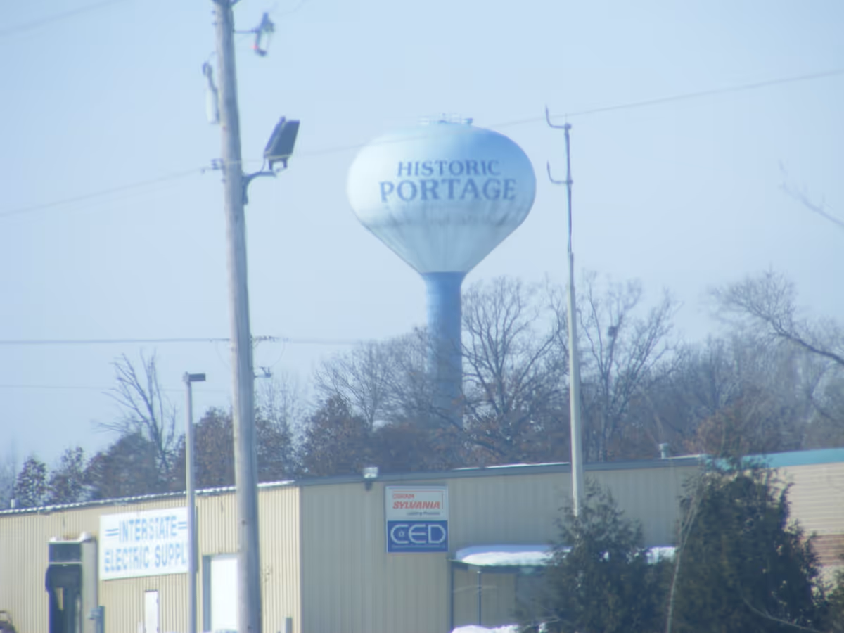 Historic Portage water tower rises above industrial buildings and utility poles in a town.