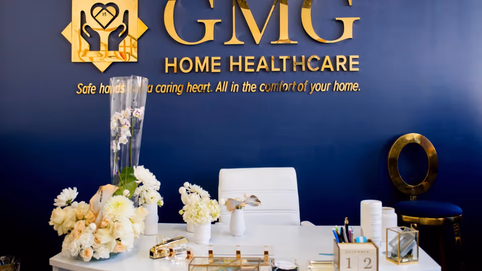Reception desk with flowers and GMG Home Healthcare logo on dark blue wall.
