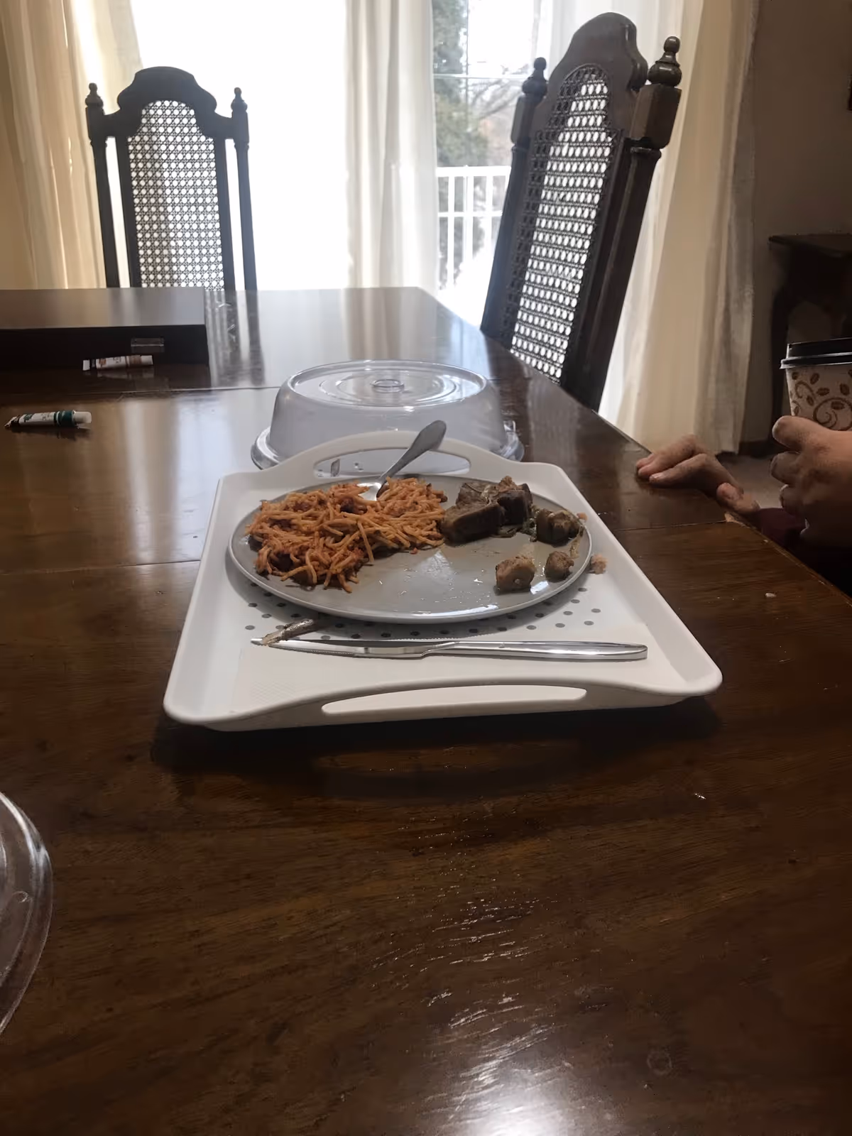 Dining table with plate of pasta and meat, silverware, and nearby hands.
