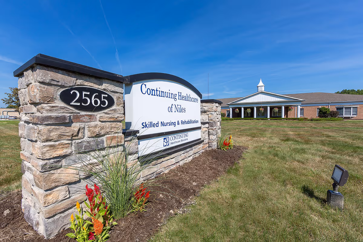 A stone entrance sign reading "Continuing Healthcare of Niles" and the address 2565 in front of a single-story brick nursing and rehabilitation building under a blue sky.