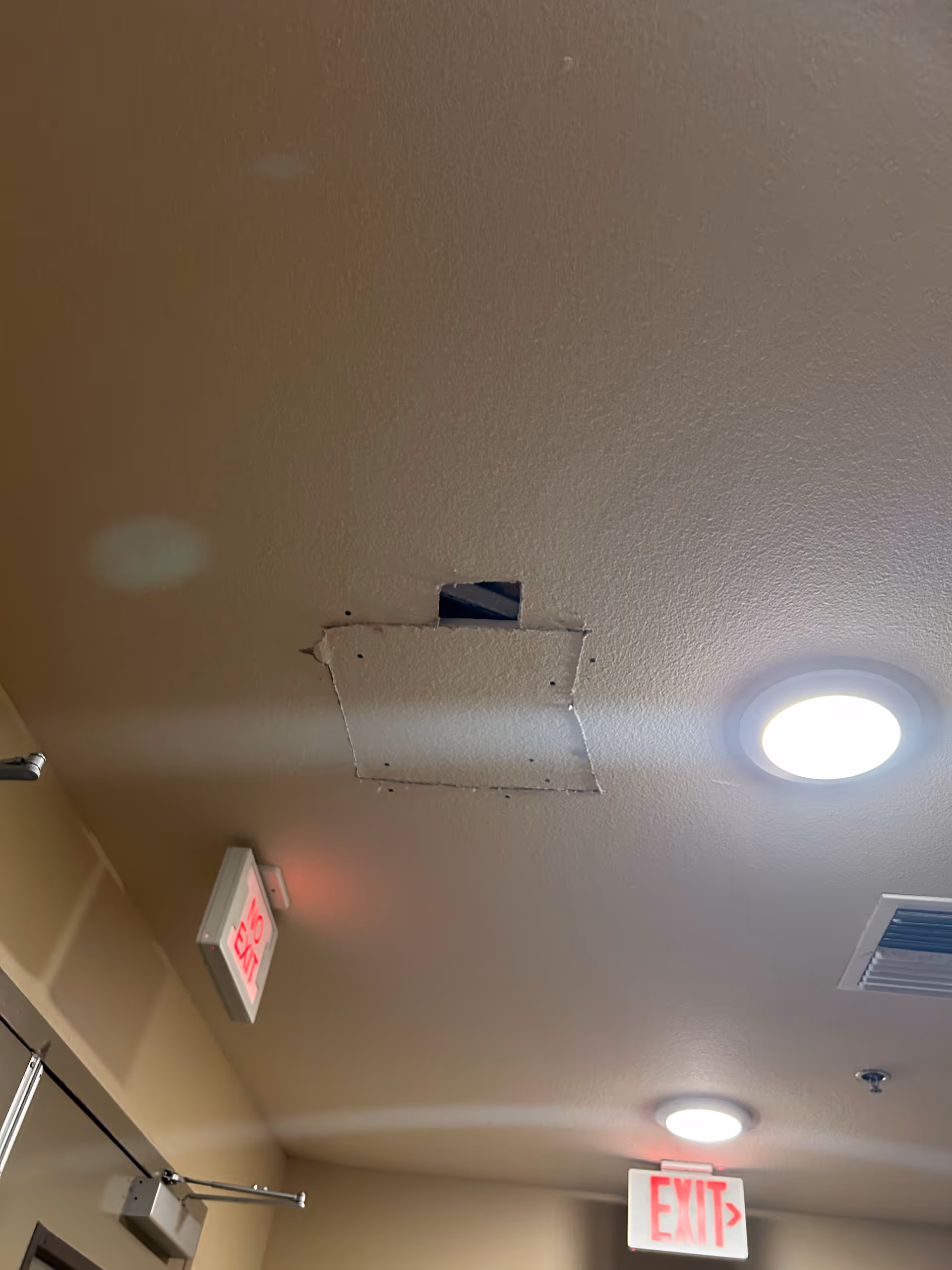 Interior hallway ceiling showing a torn panel with a dark cavity near exit signs.