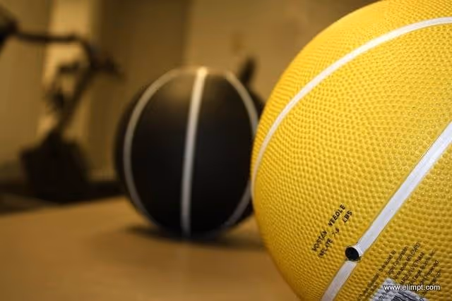 Close-up of a yellow basketball and a black ball in an indoor gym.