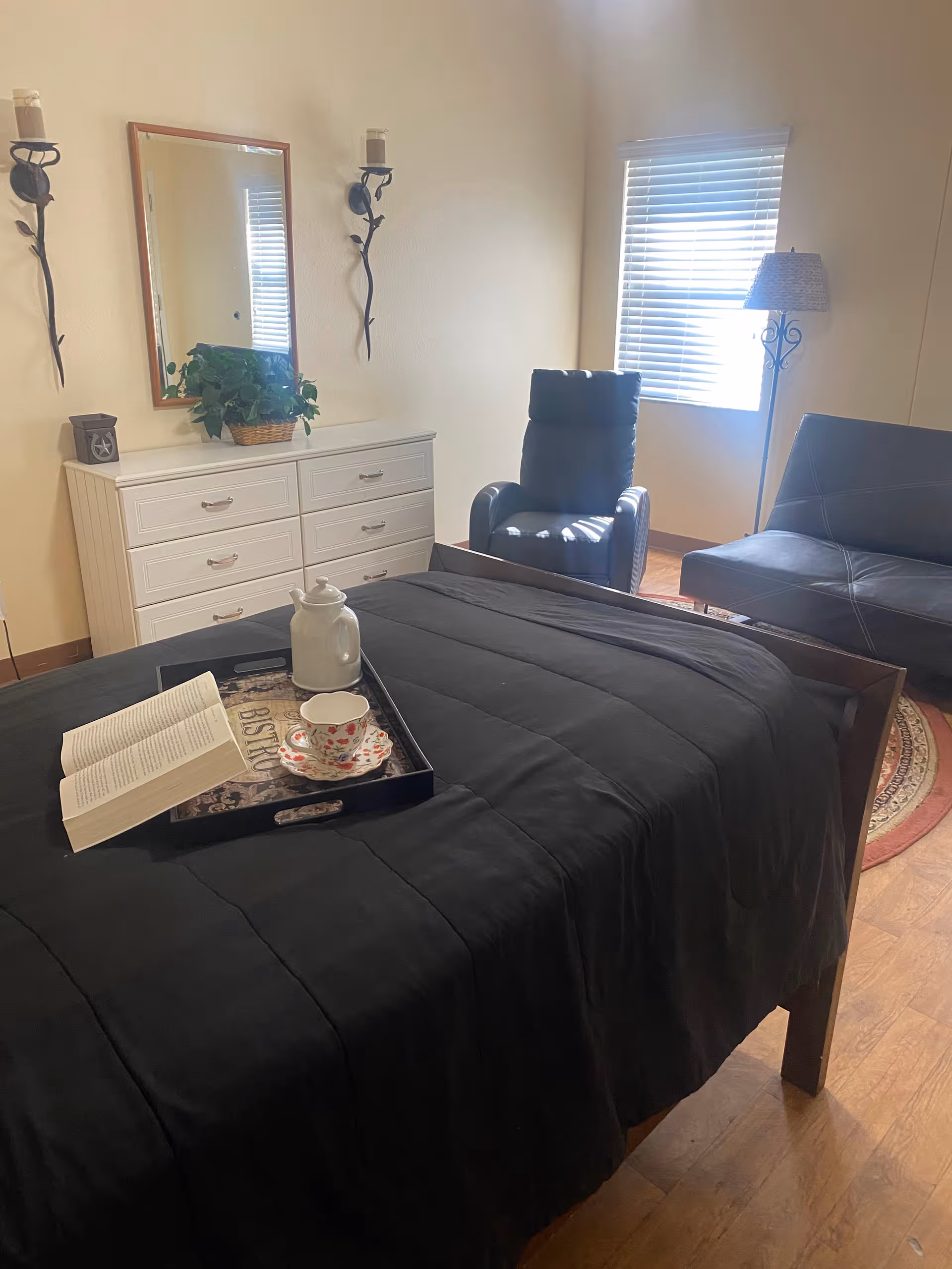A bedroom with a bed, dresser, recliner, and window blinds.