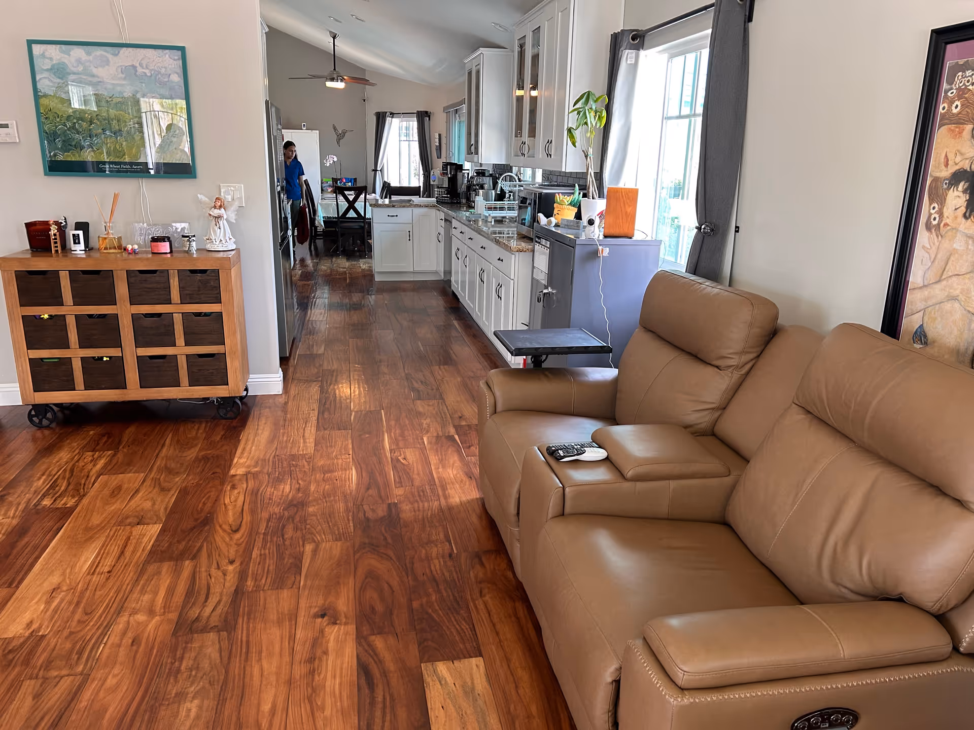 Open-concept living space with a brown leather sofa, wooden floors, and a bright kitchen.