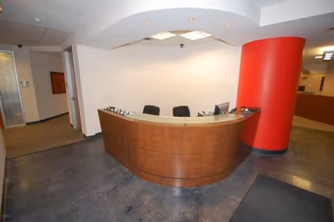 Reception desk in a modern lobby with a curved wooden counter and red pillar.