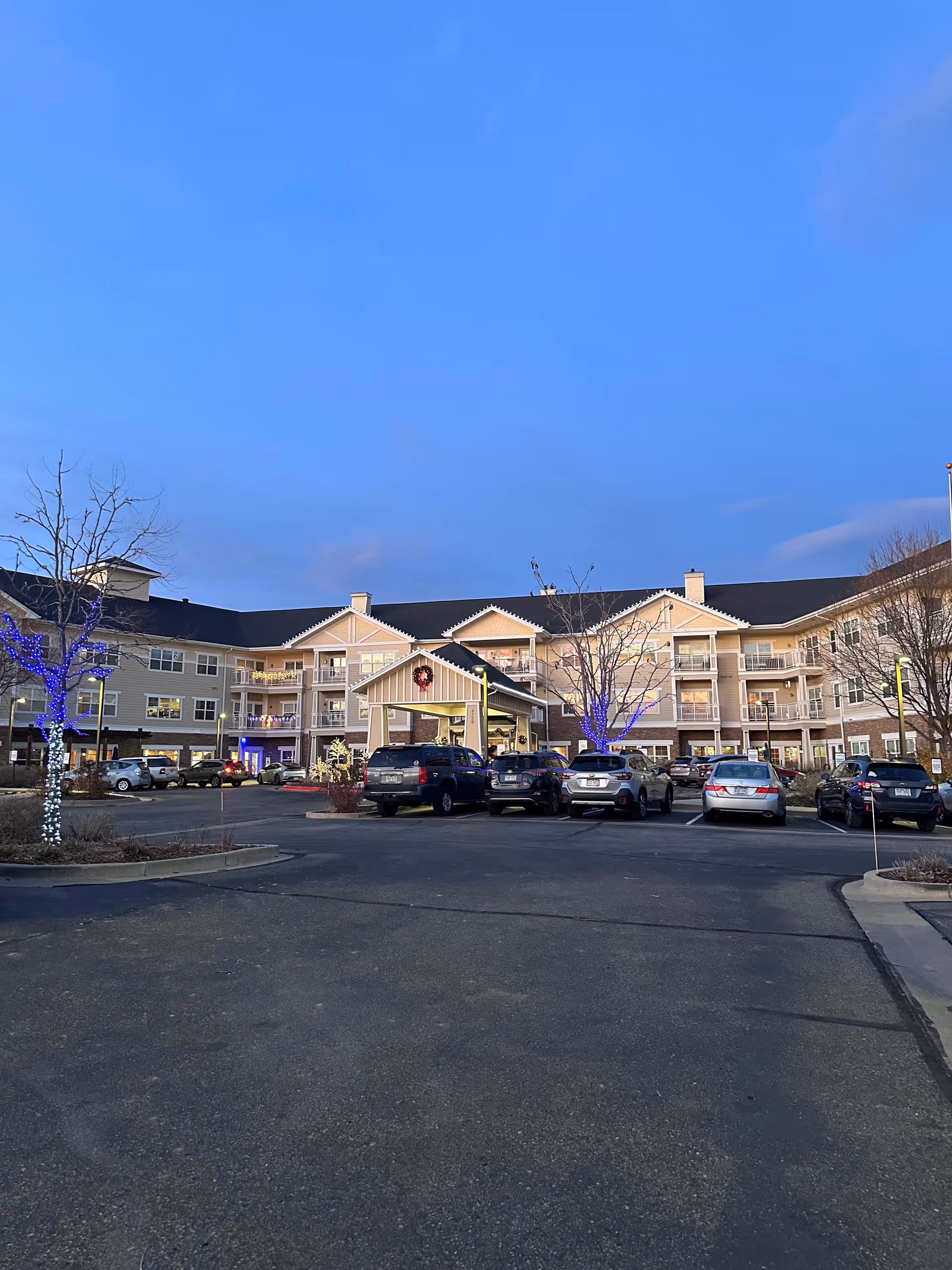 Exterior view of a senior living facility with a gabled entrance and parked cars.