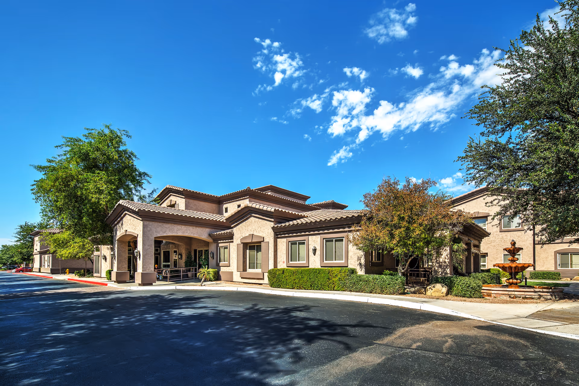 Exterior view of Ridge at the Stratford, a stucco senior living campus with driveway and fountain.