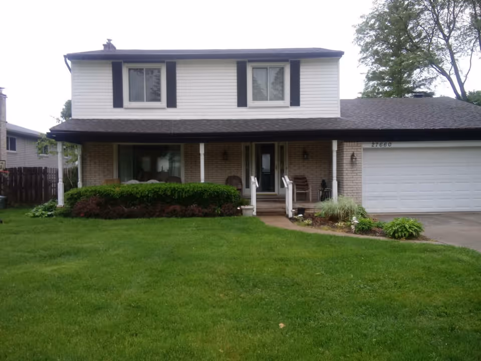 Front view of a two-story house with a porch and well-kept lawn.