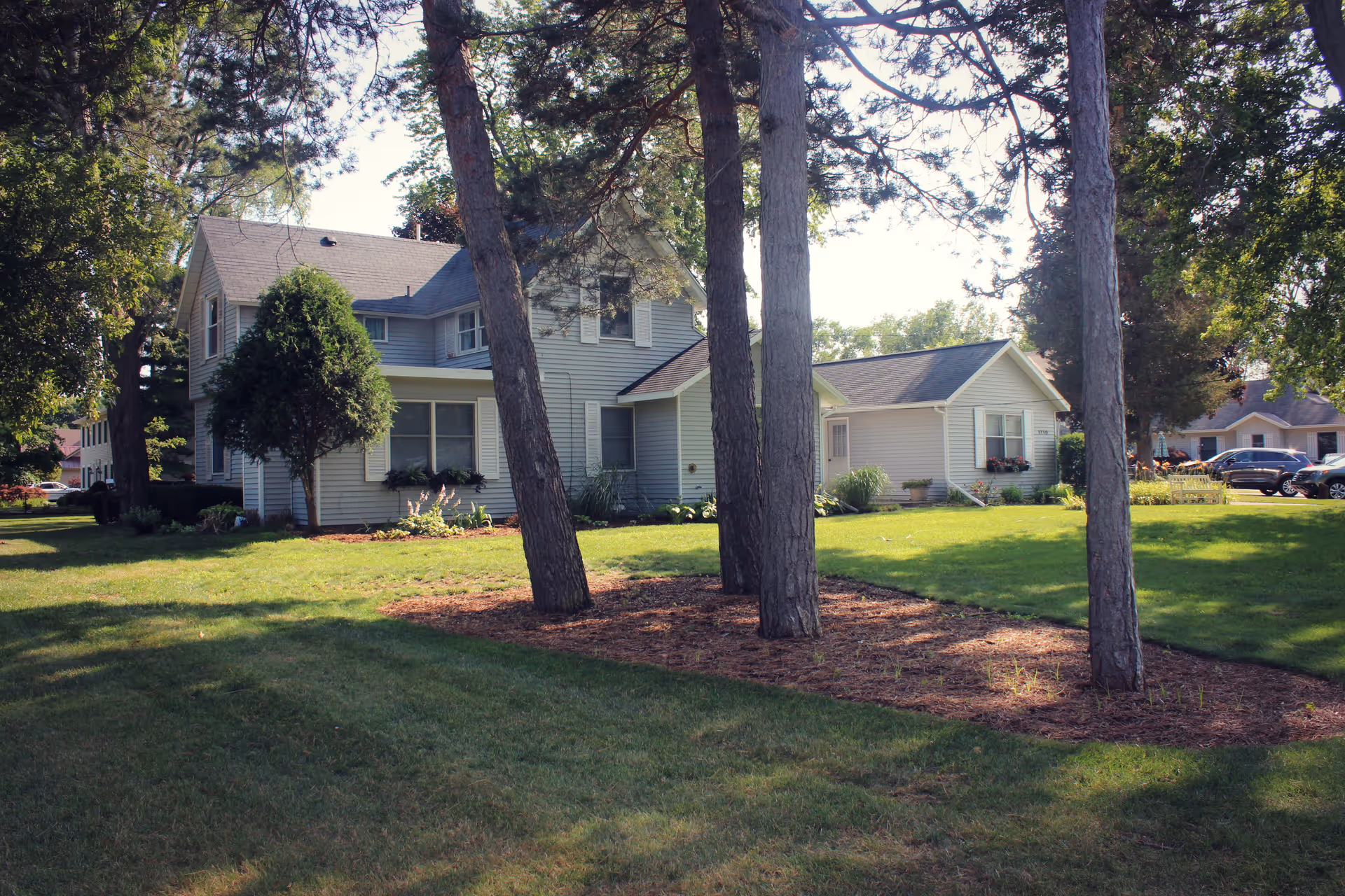 Exterior view of a light blue senior living campus building with manicured lawn and trees.