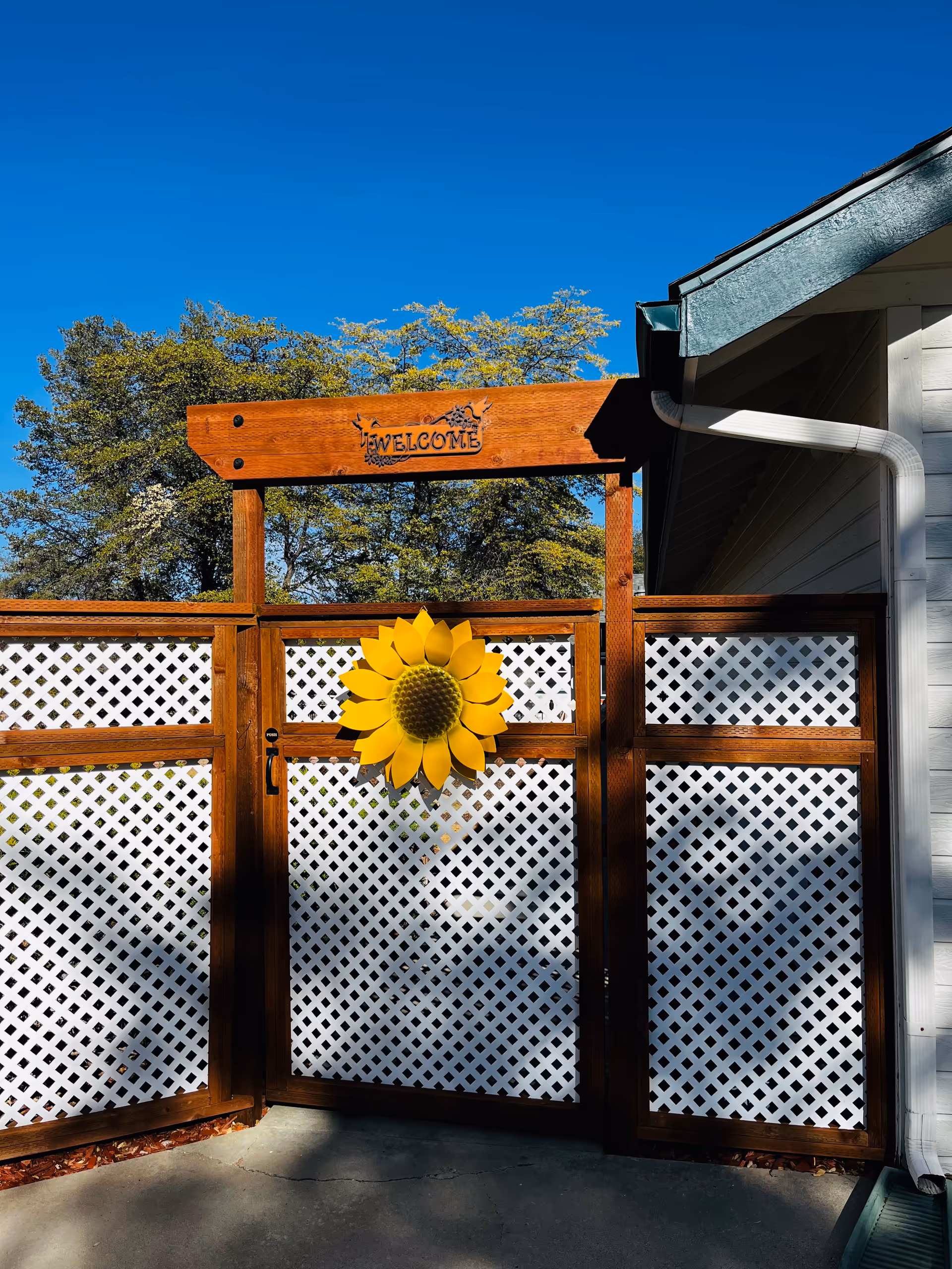 Wooden gate with a sunflower decoration and white lattice panels outside a building.