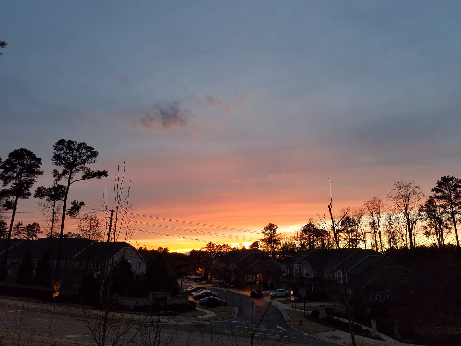 Sunset over Willow Creek Senior Living Apartments, with parked cars and tall trees along the street.