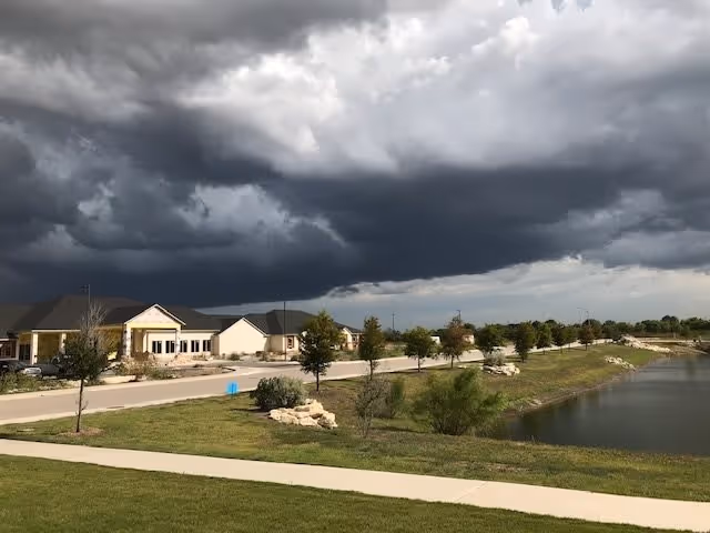 Senior living buildings along a road by a pond under dark storm clouds.