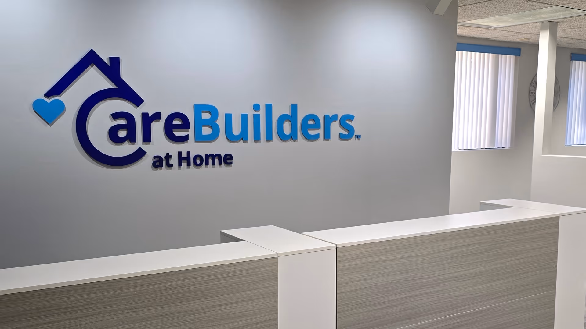 Reception desk in a CareBuilders at Home lobby with logo on the wall.