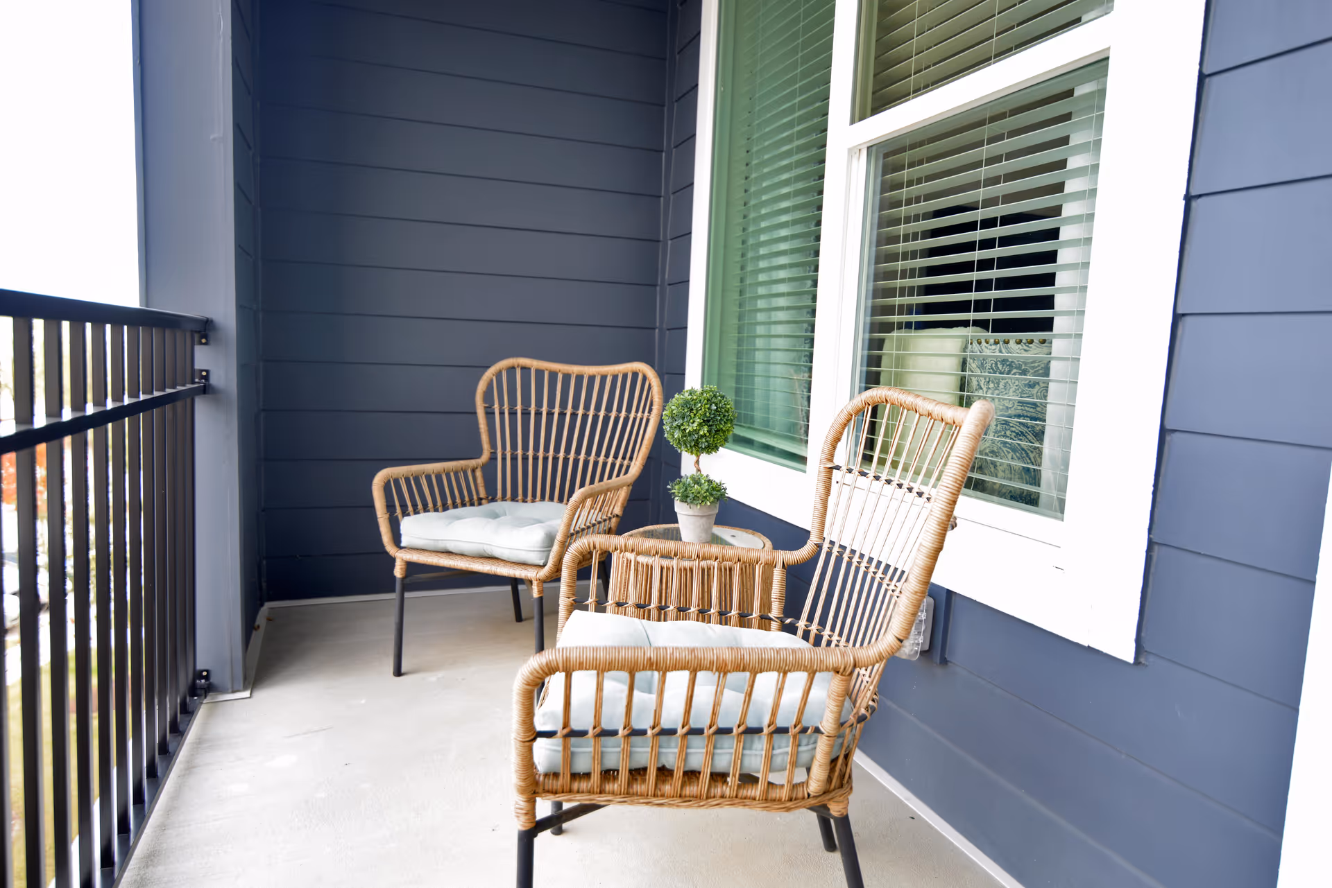 Two wicker chairs and a small table with a potted plant on a balcony.