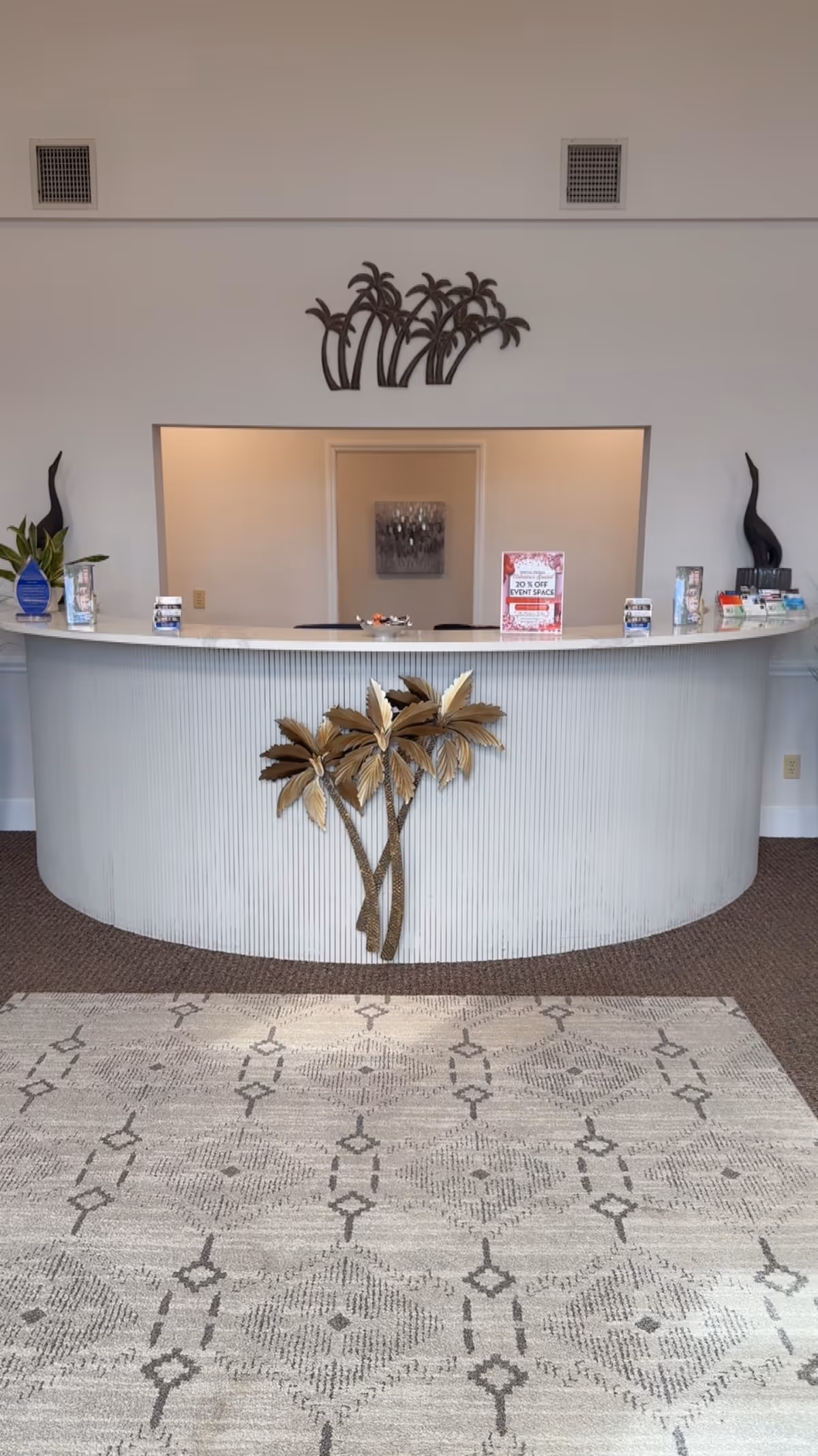 Curved reception desk in a bright lobby with a palm tree sculpture.