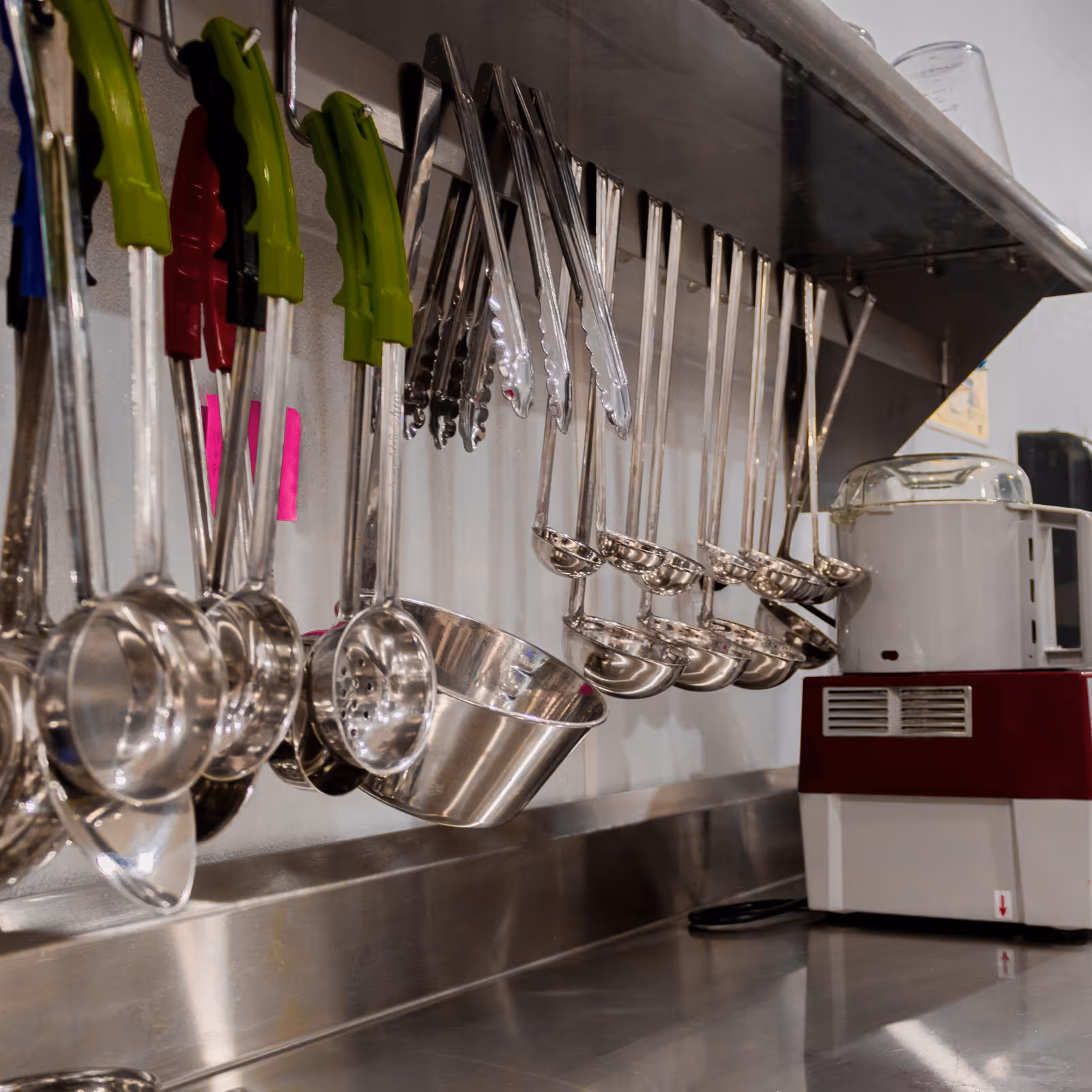 Hanging metal ladles and cups over a stainless steel kitchen counter.