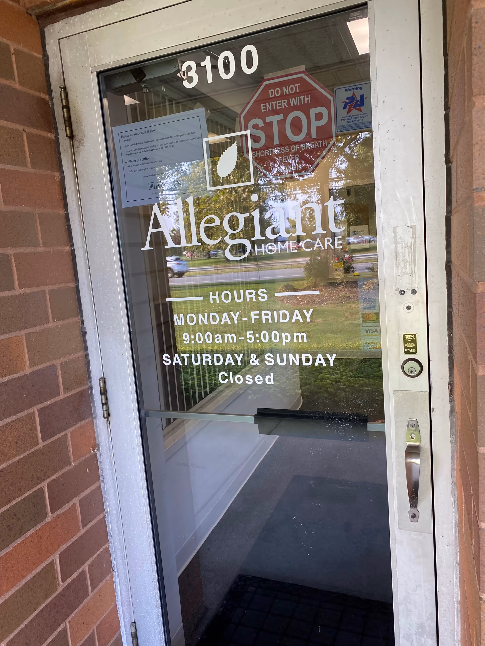 Glass entrance door with Allegiant Home Care branding and hours listed on brick exterior wall.