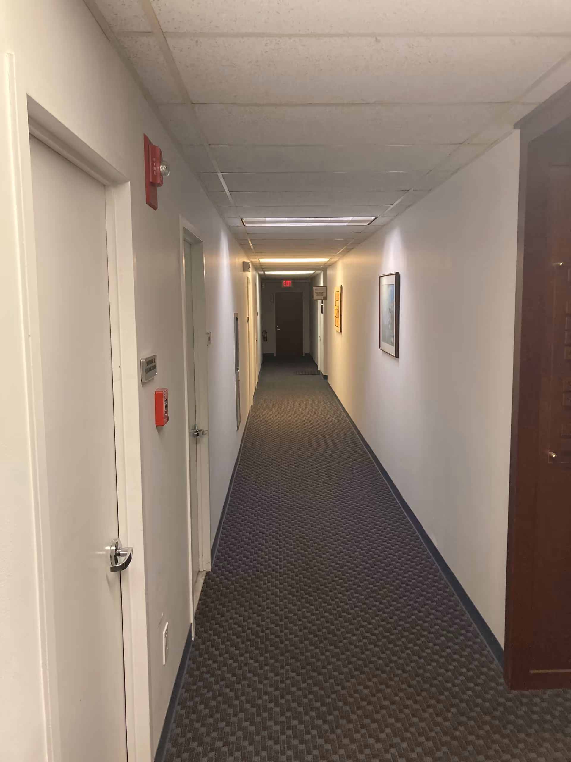Long indoor hallway in a senior living facility with doors and framed art.