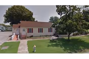 Single-story beige building with red roof, red shutters, and green lawn.