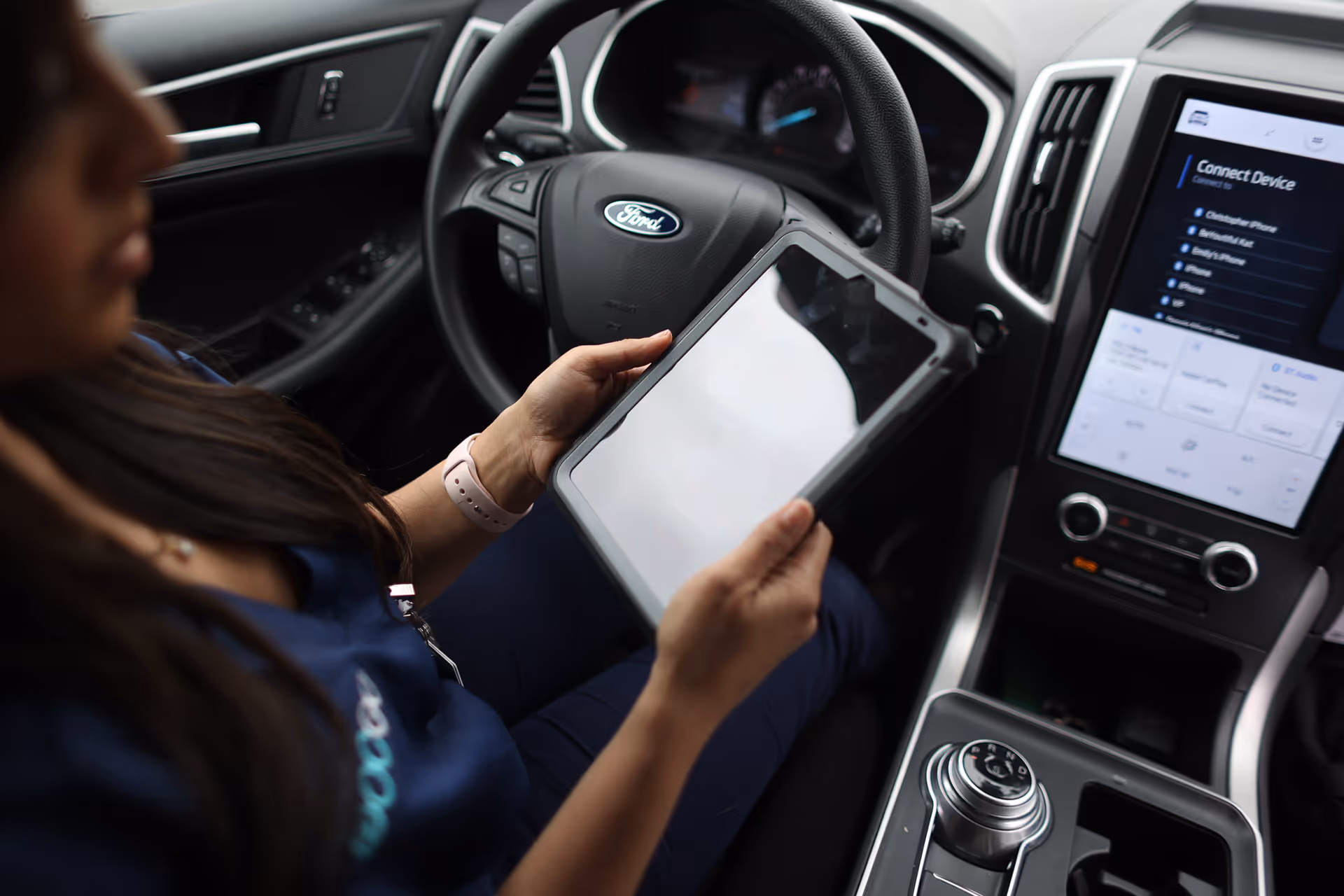 A person in a car uses a tablet near the steering wheel.