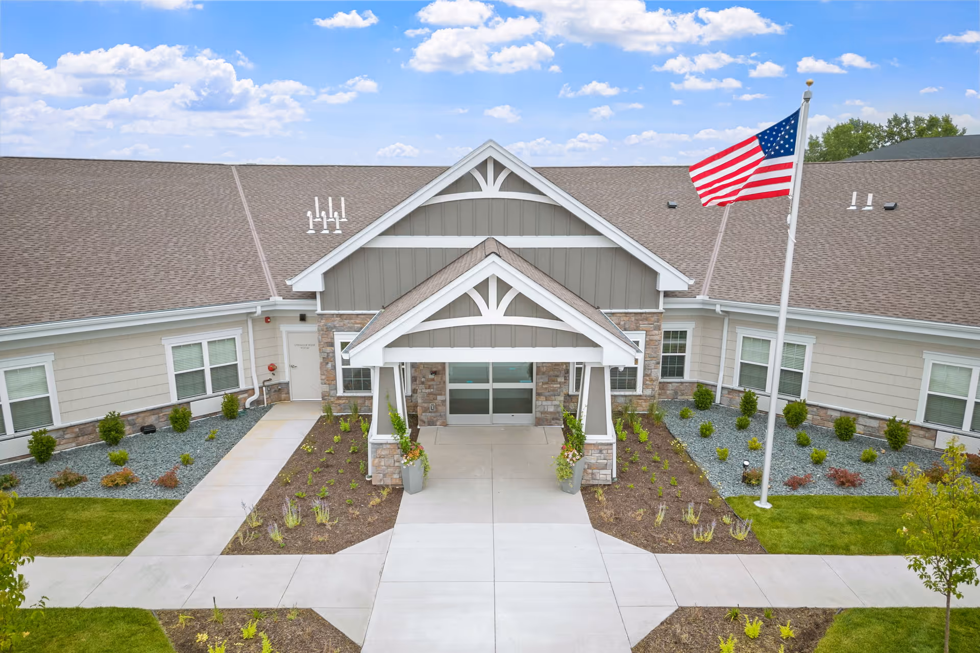 A single-story senior living facility entrance with landscaping and an American flag