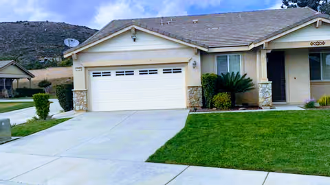 Front view of a beige house with a two-car garage and green lawn.