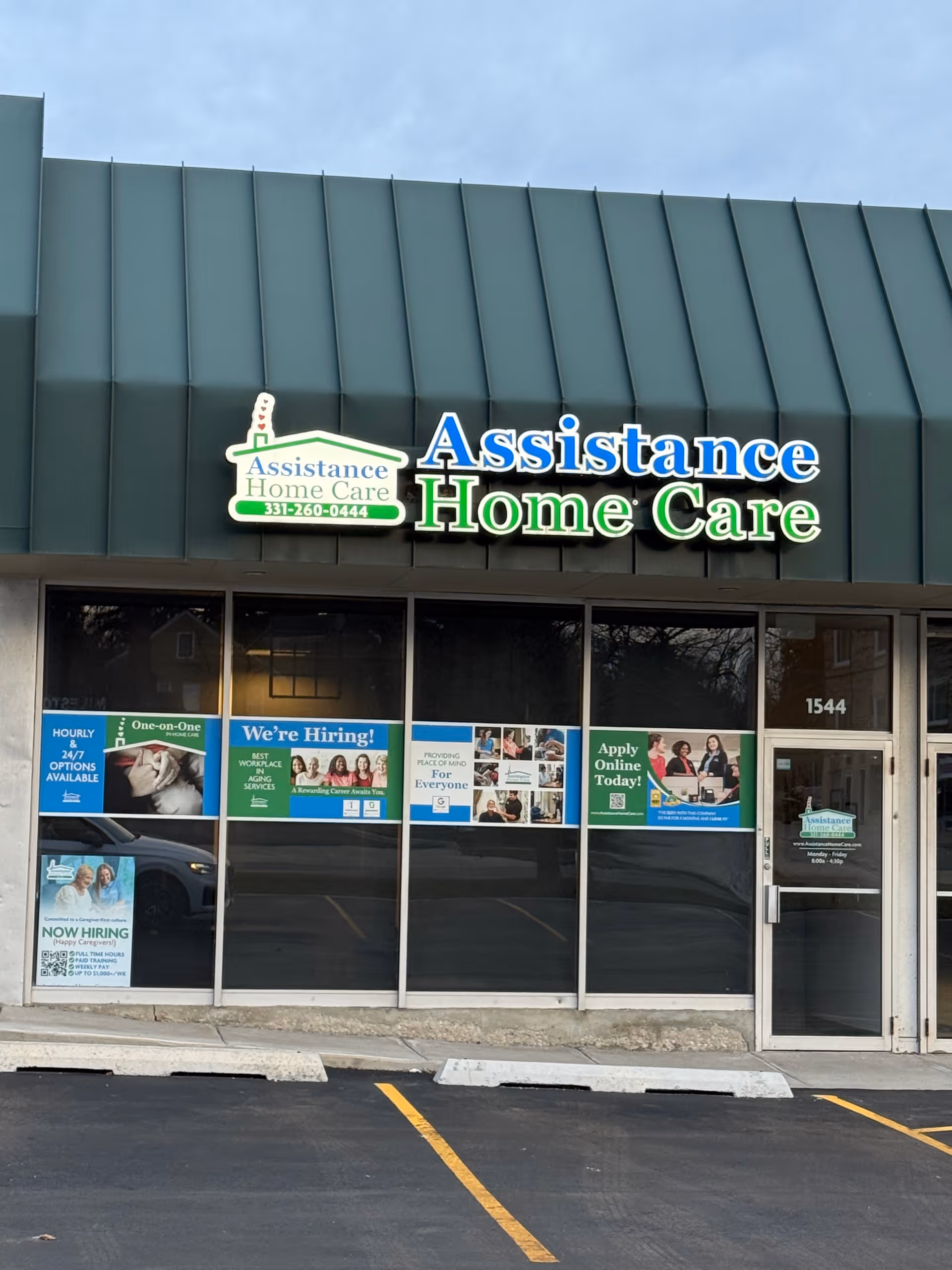 Front exterior of Assistance Home Care storefront with large sign and hiring posters in windows.