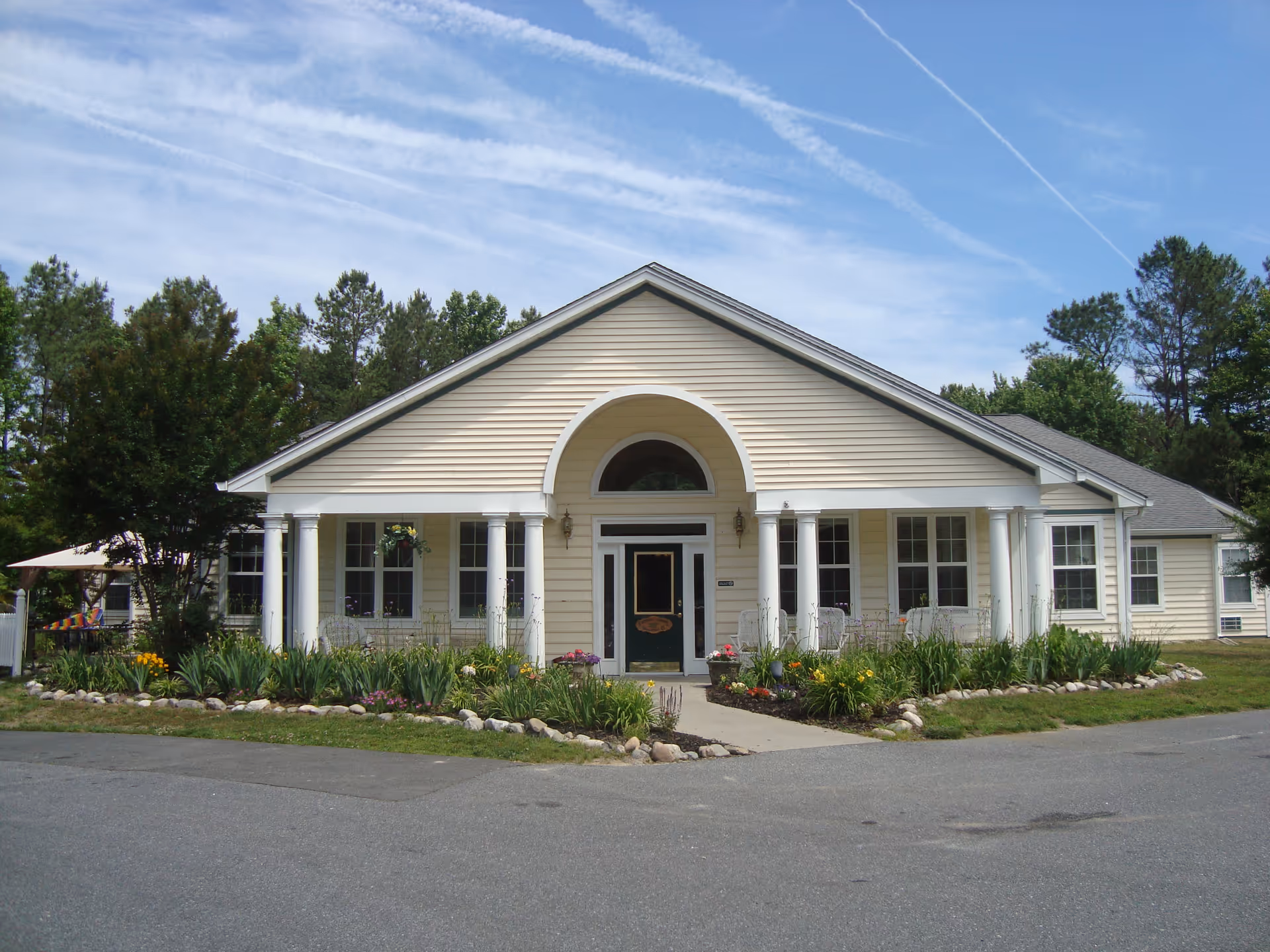 Front view of a cream-colored senior living facility with white columns and landscaped gardens.
