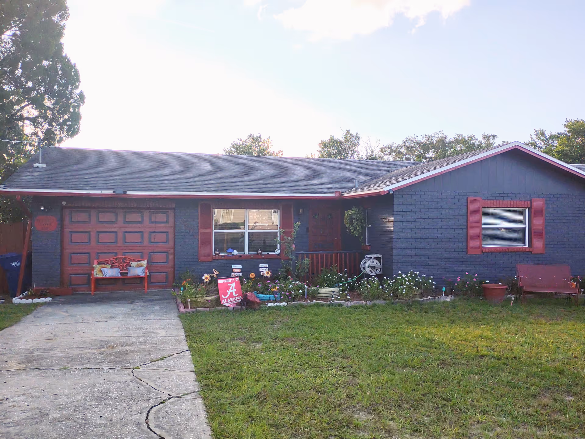 Blue-gray single-story house with red trim, closed garage, and small front-yard garden.