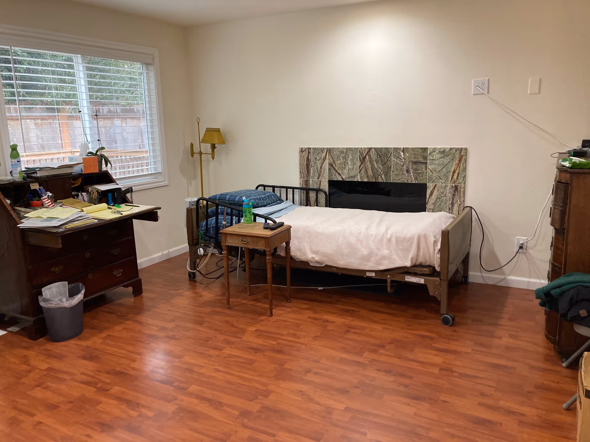 A simple bedroom with a single bed, cluttered desk, and wooden floor.